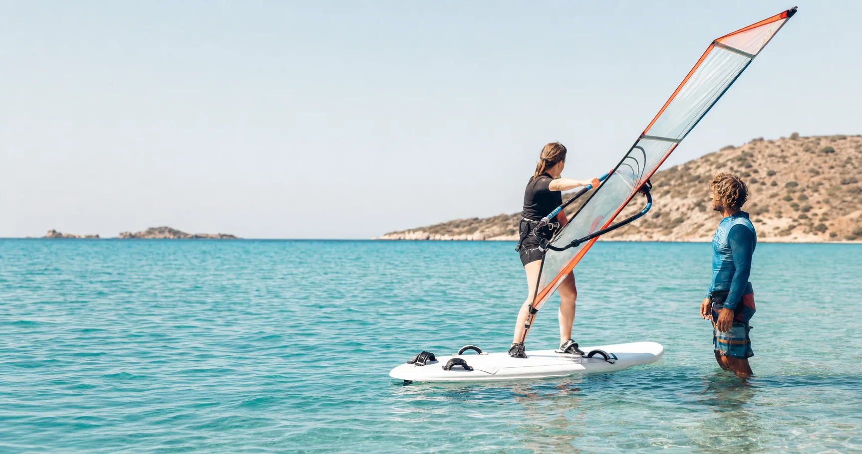 Sığ denizde eğitmen eşliğinde windsurf çalışan başlangıç seviyesinde bir öğrenci